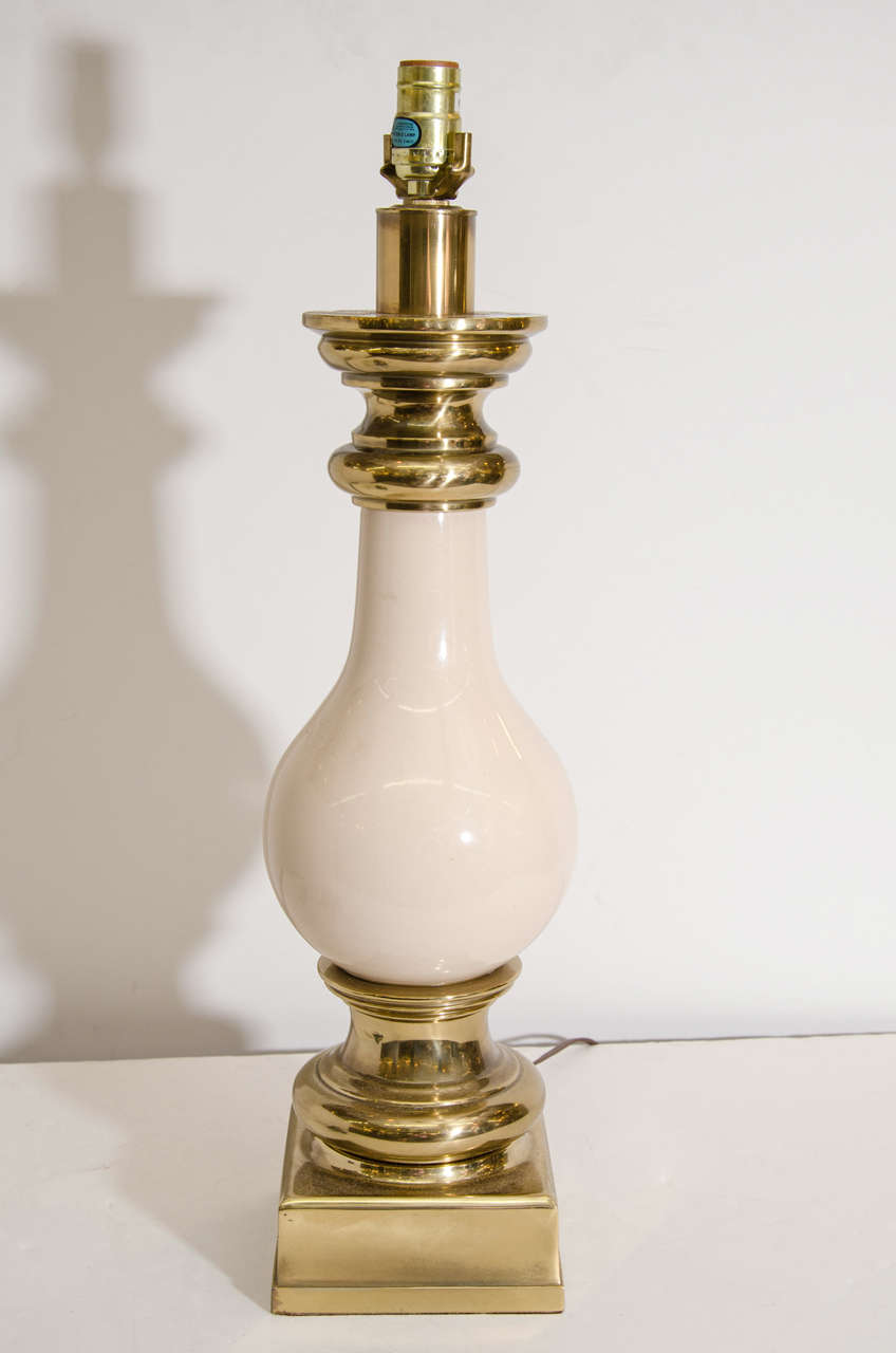 A pair of vintage table lamps with cream colored ceramic bodies and brass accents. They retain their Stiffel sticker labels on the sockets.