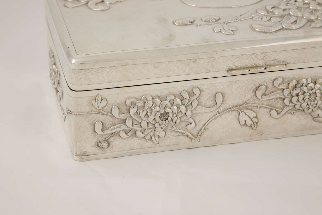 A large Chinese export silver table or cigar box, embossed on five sides with chrysanthemum against a matte background. The hinged lid has a plain oval vacant cartouche to the centre. The box measures 24.5cm x 14.5cm x 8cm and weighs 1327gms.
It
