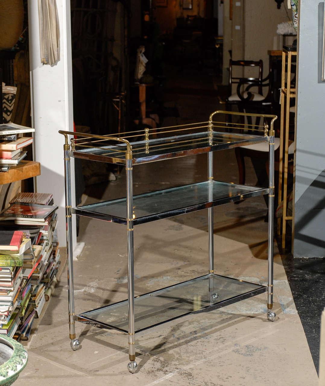 Mid Century Bar Cart of steel with a brass gallery and brass accents.  The cart holds three glass shelves and is supported by casters.