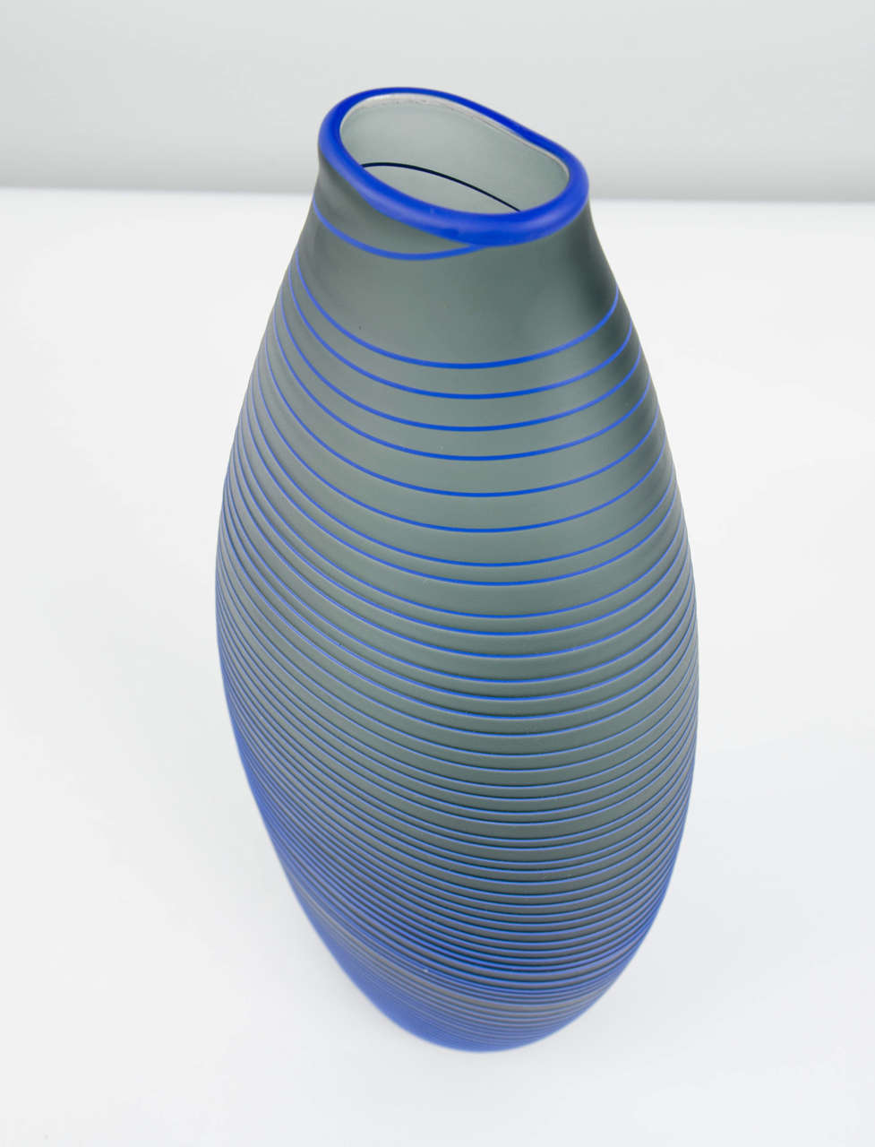 Tonal Frequency Vase in Grey is a unique handblown glass vessel with fine raised cane detail created by the British artist Liam Reeves. Handblown in grey glass, the exterior surface has a blue glass trail that winds around the entire piece, ending