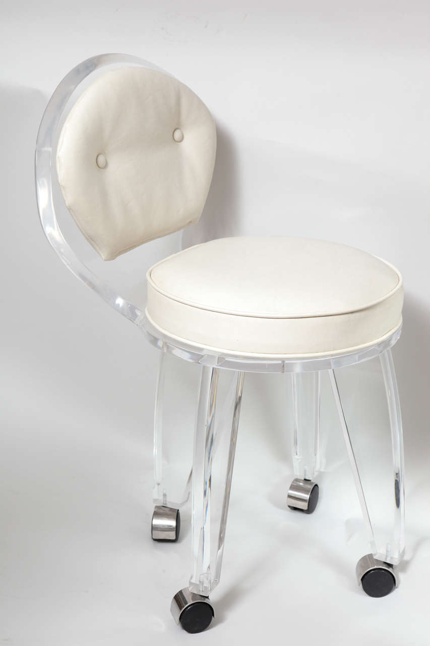 An elegant vintage Lucite vanity swivel chair with white vinyl upholstery. This practical piece would work great for any vanity or desk and is on a good set of rolling casters.