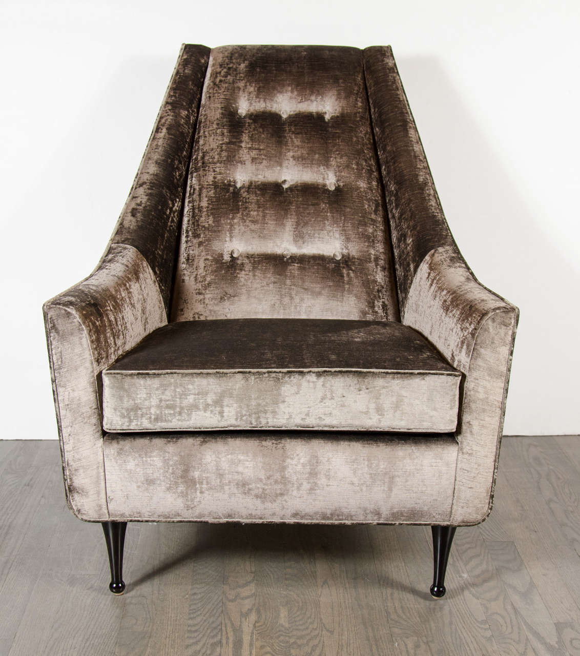 This luxurious chair features a cylindrical form tapered leg in ebonized walnut and has been newly upholstered in a smokey grey velvet. The chair also features button back detailing and the modernist design of the chair is sleigh form. This chair