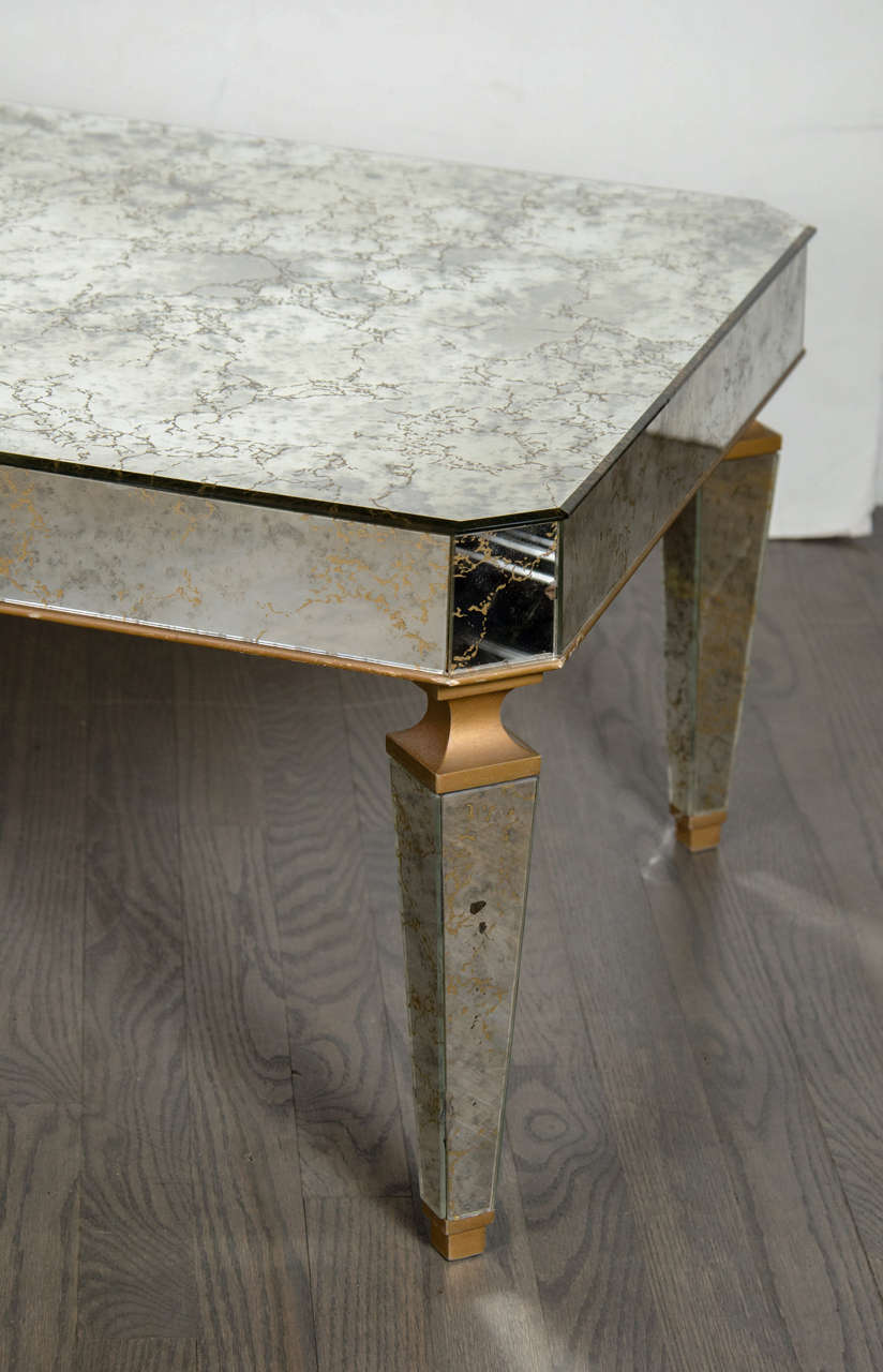 This gorgeous and glamorous Hollywood regency cocktail table was realized in France, circa 1945. It features antique gold vein mirror with gilt detailing; a tapered leg design; and gently rounded edges. With its monochromatic palate and clean