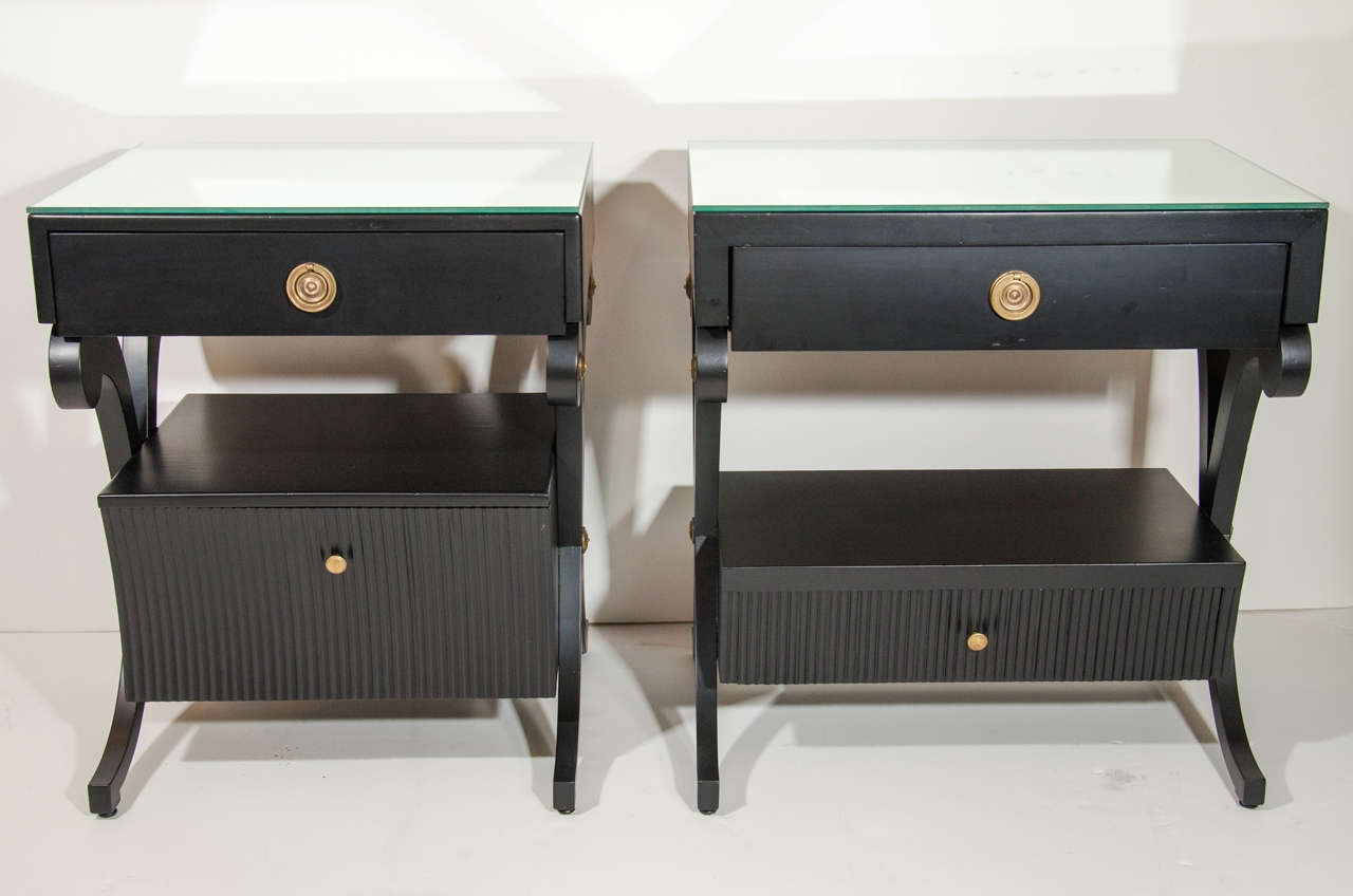 Elegant pair of Hollywood Regency nightstands or end tables in a satin black lacquer finish, with stylized bronze mounts and fittings. The tables are a companion set and have slightly different dimensions. The tables feature stylized scrolled leg