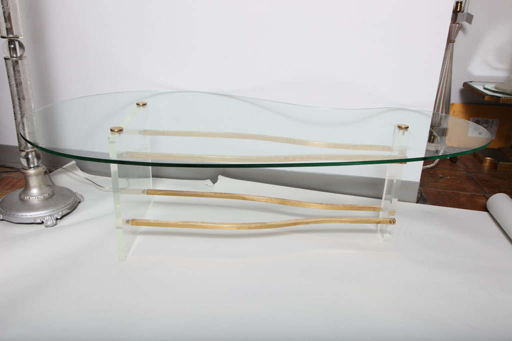 An 'invisible' glass kidney form table secured on a plexiglass and brass rod base. Chip to edge