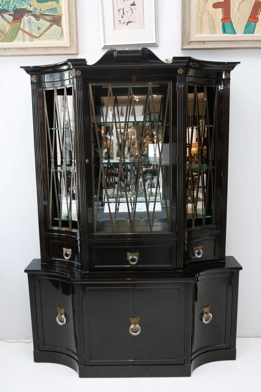 A beautiful lacquered ebony Regency style cabinet by Grosfeld House with unique brass and Lucite hardware. The lighted display cabinet at the top has glass shelves and brass diamond-patterned mullions and is mirror-backed. The center door has a