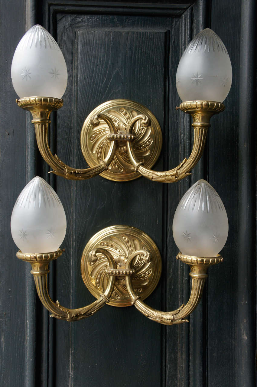 These early 20th century French Louis XVI style two-arm sconces are cast in bronze and once graced a home as exterior lighting as indicated by the color and patina on the reverse. Now fully polished and lacquered the sconces are cast with fine