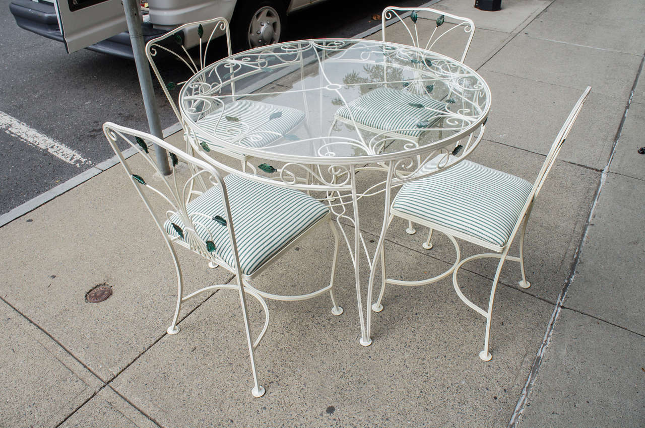 This lovely set from circa 1950 to 1960 is in great shape. The set has been freshly painted and upholstered and has a new glass top as well. The set consists of a table and four chairs. The design is of a veining trail of leaves set within the iron