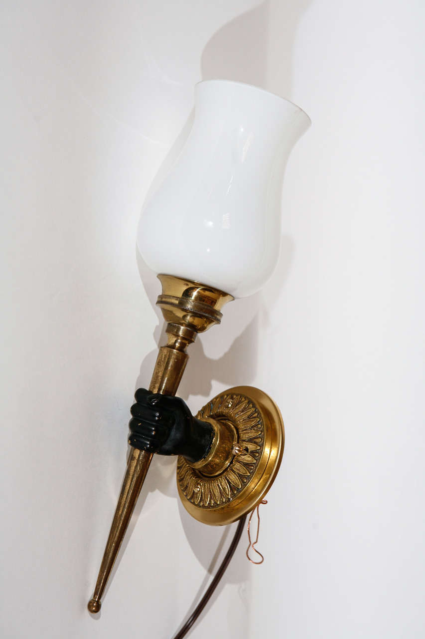 A single French neo classical bronze sconce, featuring a black hand holding a torch sconce.  This sconce has amazing detail on the plaque that attaches to the wall. White glass shade.