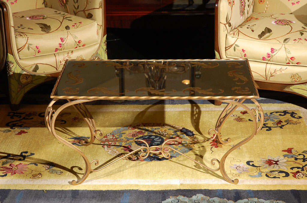 Zarter Couchtisch aus Frankreich, ca. 1930er Jahre. Der Tisch hat einen blattvergoldeten Rahmen aus Schmiedeeisen und eine rückseitig lackierte Spiegelplatte mit Akanthusblattmotiv.