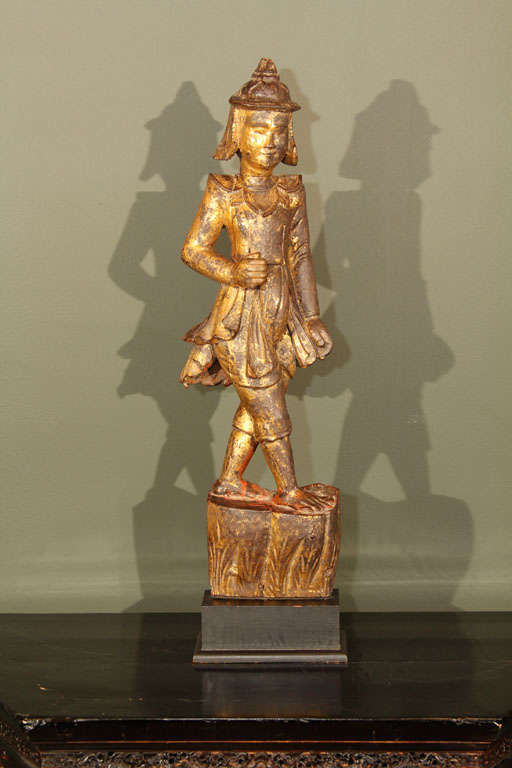 Burmese carved, lacquered and gilt wood figure of a standing soldier. Dressed in the traditional Burmese uniform with topcoat, pants and helmet, the figure depicted with arms at his side and one foot in front of the other as if marching in a