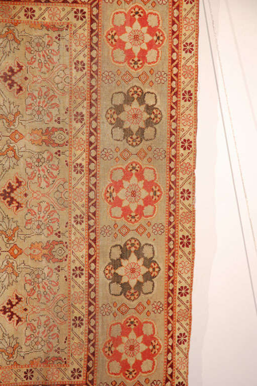 A border with stylized flowers of alternating color encloses a field of repeating spreading palm displays in this Amritsa Antique Indian Rug of warm contrasting tones. Pale green, mustard yellow, red and black predominate.