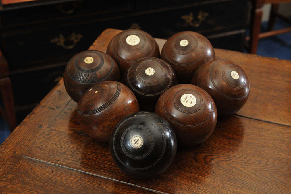 Each weighted wood ball, in black or brown, inlaid with ivory discs engraved with club monograms and numbers surounded in incised trim. Eight available