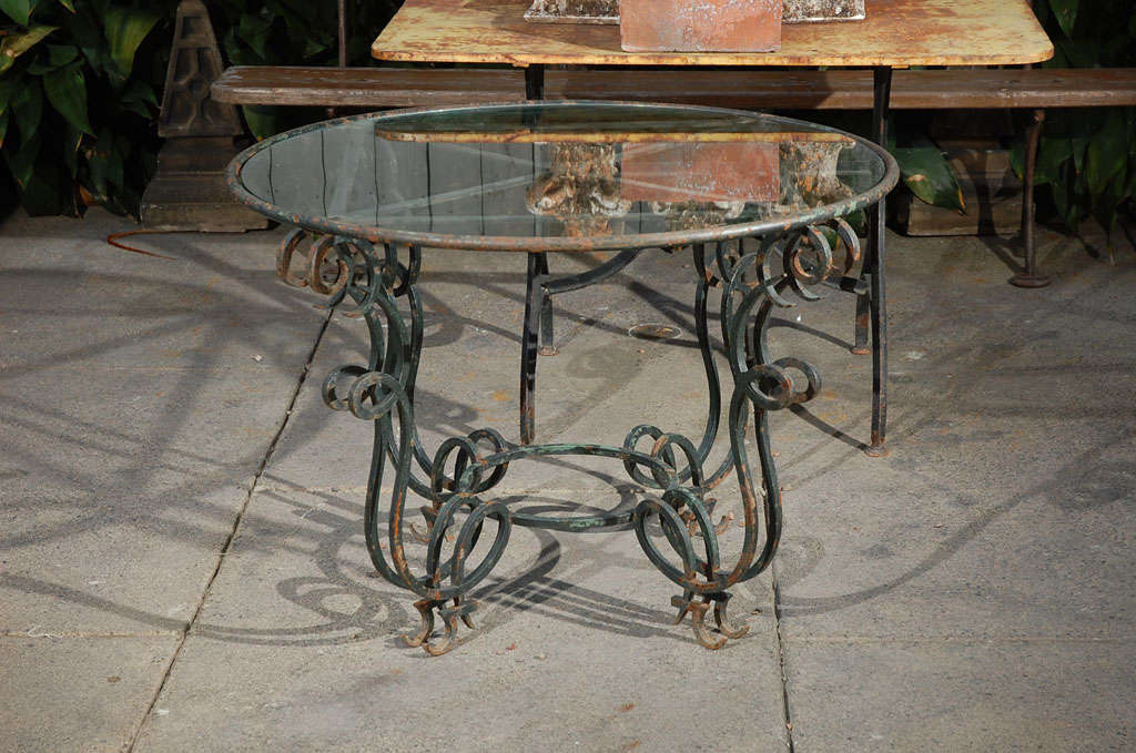 A round glass-top table with a unique scrolling iron base. Great garden table, dining table or occasional table.