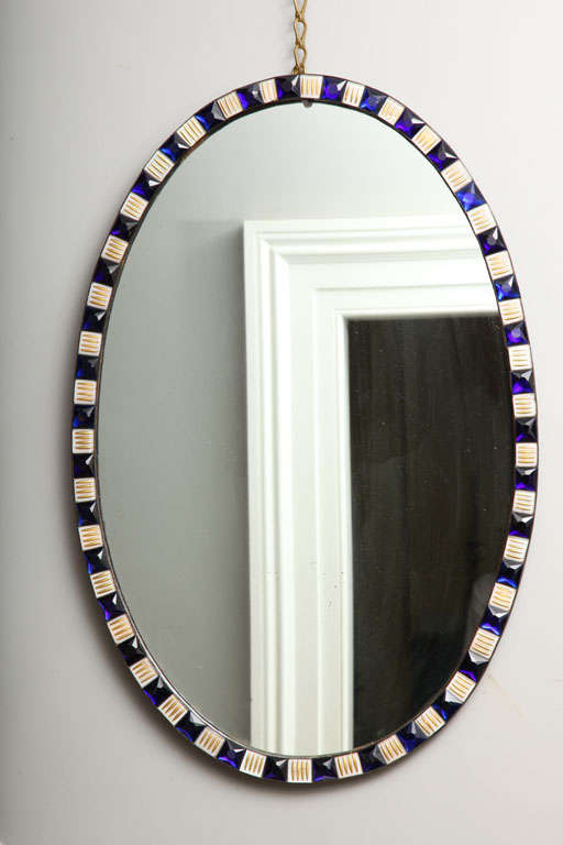 Fine and rare Irish oval mirror, the copper frame with faceted ring-set sapphire blue glass jewels alternating with white and gilt enameled jewels centring the original silvered plate, circa 1785.