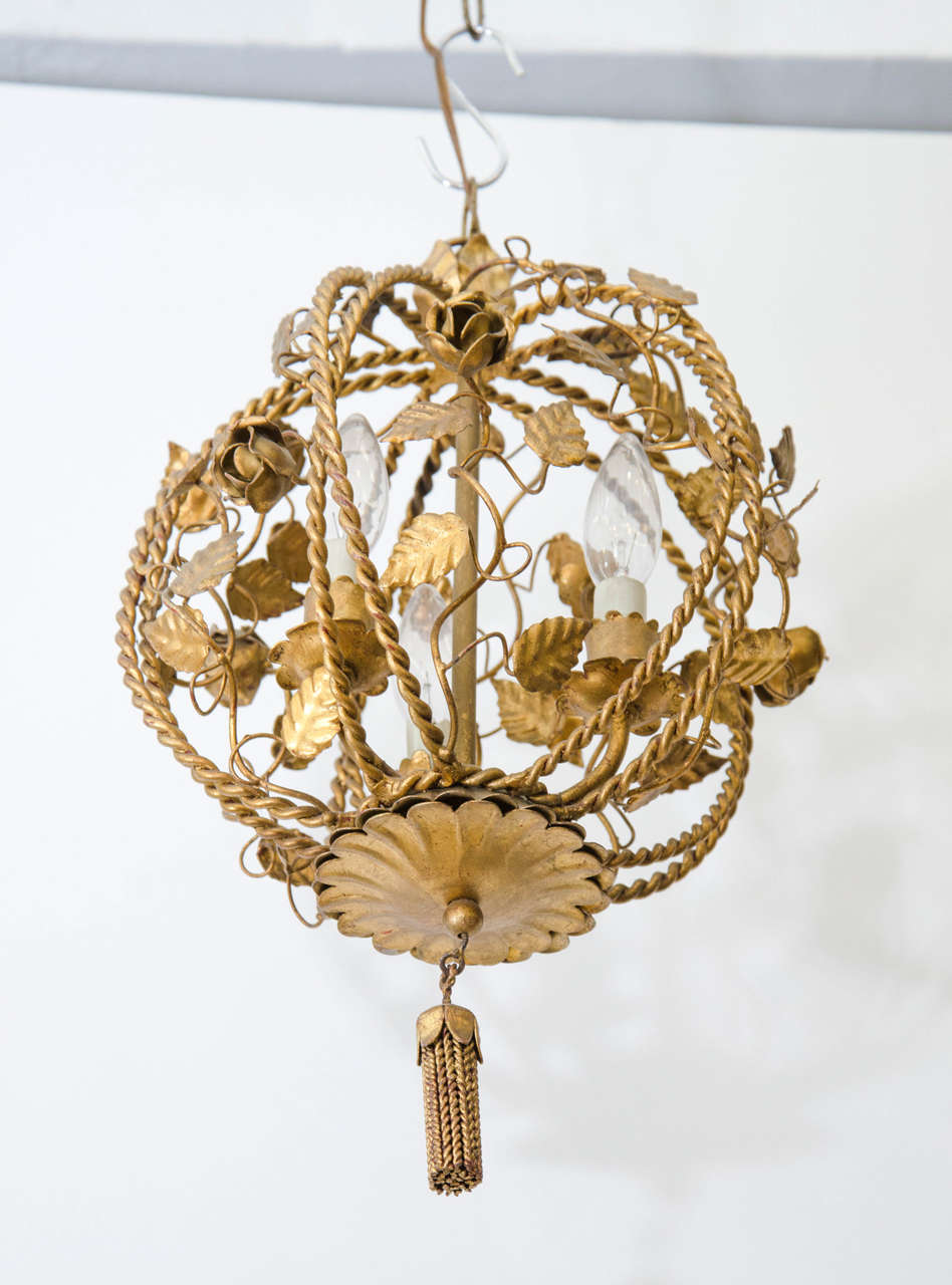 A vintage petite three-light chandelier in brass with flower and leaf motif. A tassel dangles from the bottom. Good vintage condition with age appropriate patina. 