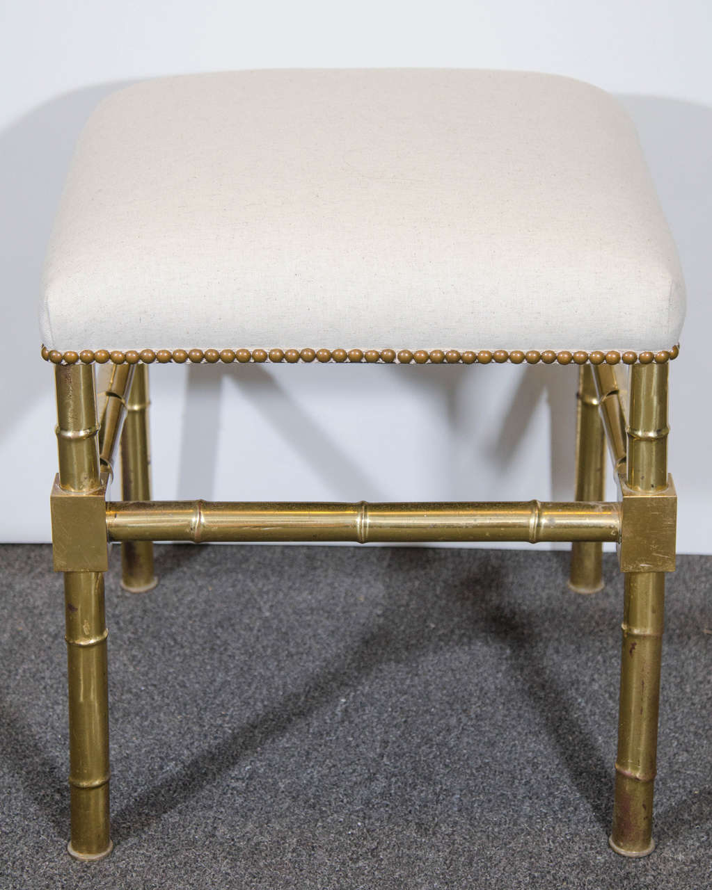 A vintage pair of Italian brass faux bamboo stools or ottomans newly upholstered in a sand colored linen with nail head detailing. Marked, 