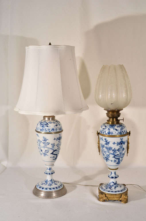 Meissen Blue Onion pattern, made from early 1700s to date. These lamps are early 1800s. On right, oil lamp not electrified is mounted on cast bronze base adorned with Egyptian Sphinx. On left, electrified oil lamp is a later time period. Lamps are