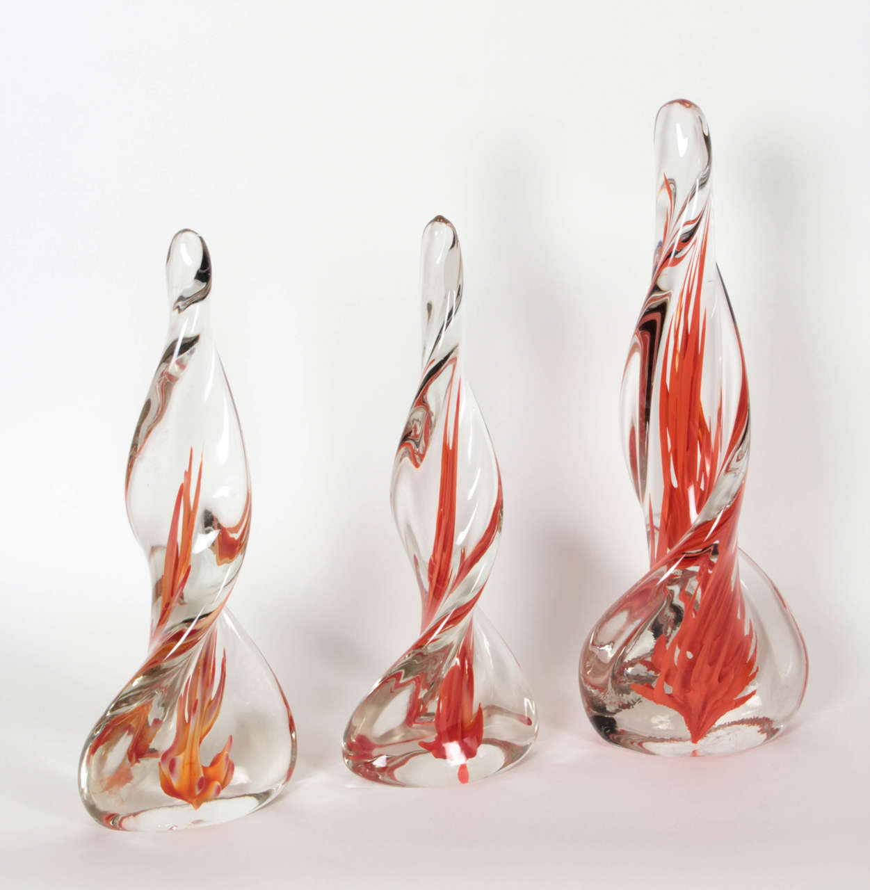 A set of three spiraling clear-glass obelisks with red flame-like intrusions by Venini. All bearing faint acid-etched stamps that date them to the 1950s.  They are 17, 14 1/4, and 14 inches tall each, and the bases are 6 1/2, 5 1/2, and 5 inches