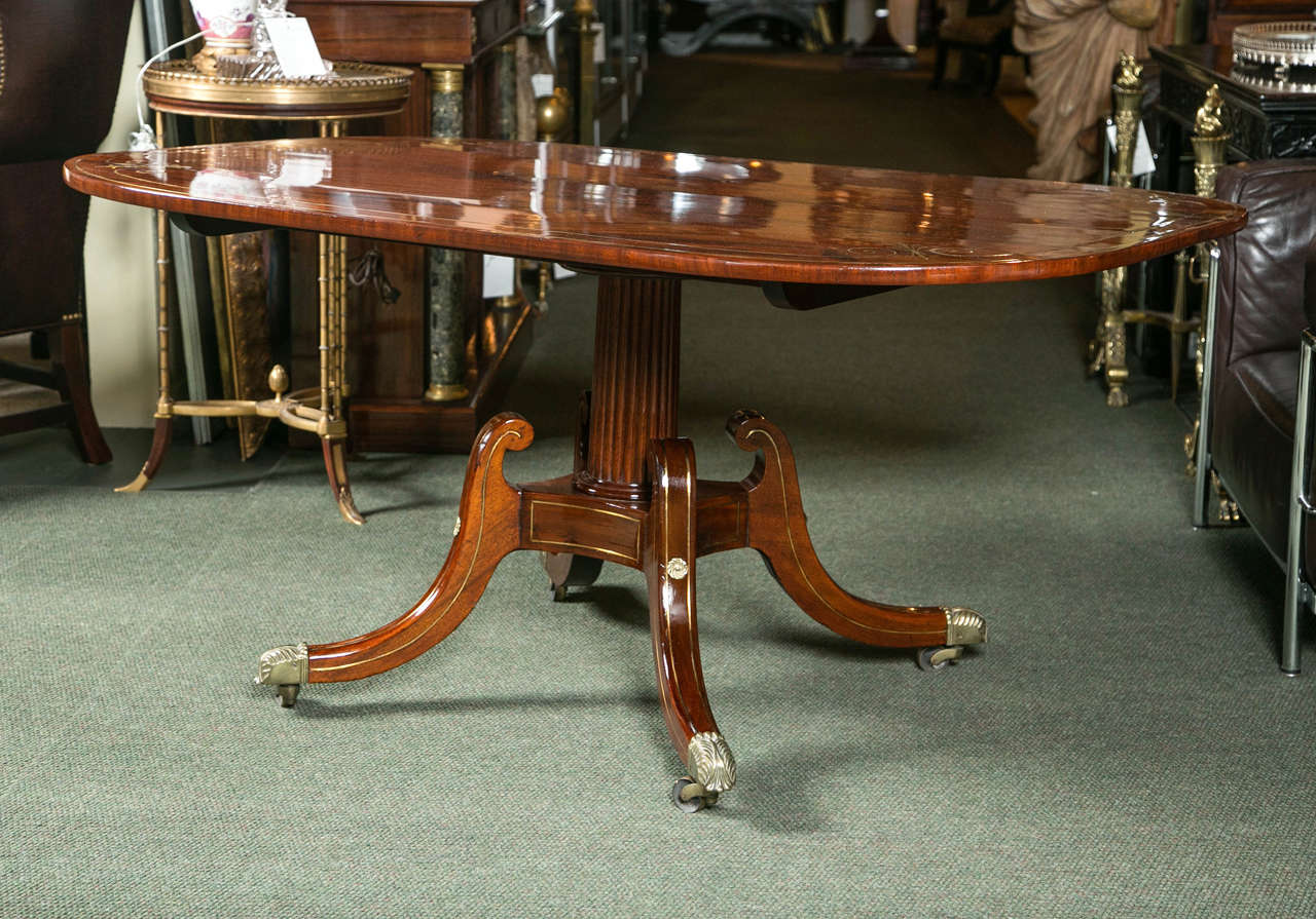 A book-matched crotch, flame, Caribbean mahogany brass inlaid Regency tilt-top breakfast table. The rectangular top surmounts a reeded pedestal supported by four splay legs of swan neck form. All terminating on bronze caps and casters. Restoration