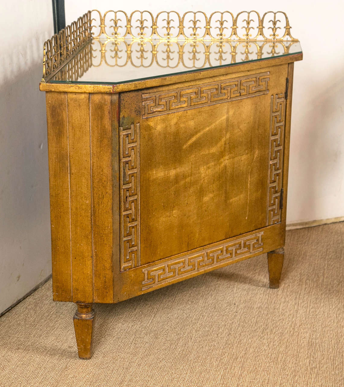 An early 20th century French glass top corner cabinet with bronze gallery, chamfered sides, stylized Greek key pattern all on raised, square tapered legs.