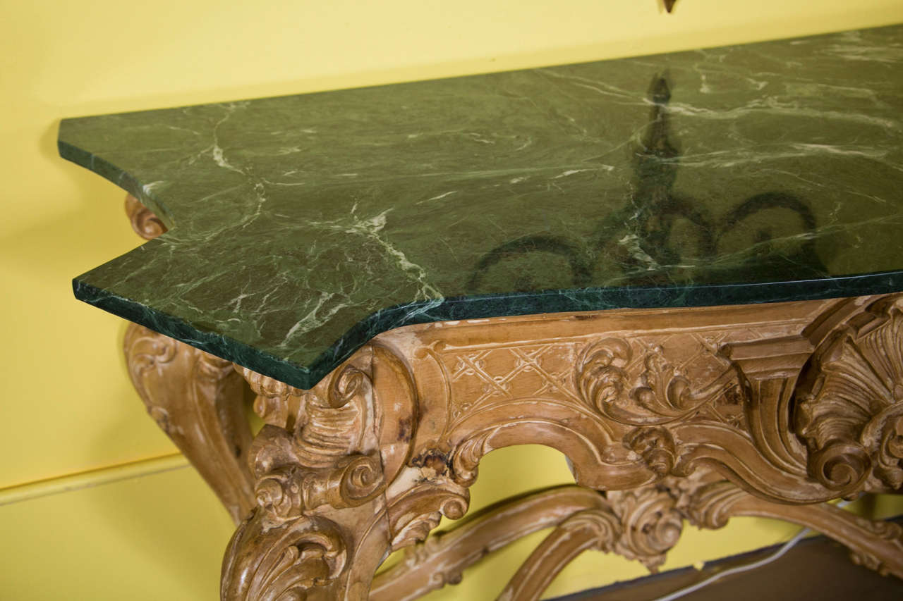 Pair of exceptional bleach wood console tables, circa 1940s, the shaped dark green marble atop an elaborately carved base, decorated with cartouche, shell, scrolls, foliate motifs, raised on cabriole legs joint by an X stretcher. By Maison Jansen.