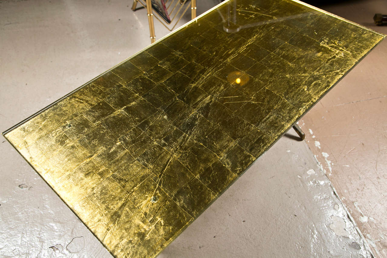 A chic coffee table of Hollywood Regency taste, the gold-leaf rectangular glass top supported on a gilt-brass base with a magazine shelf.