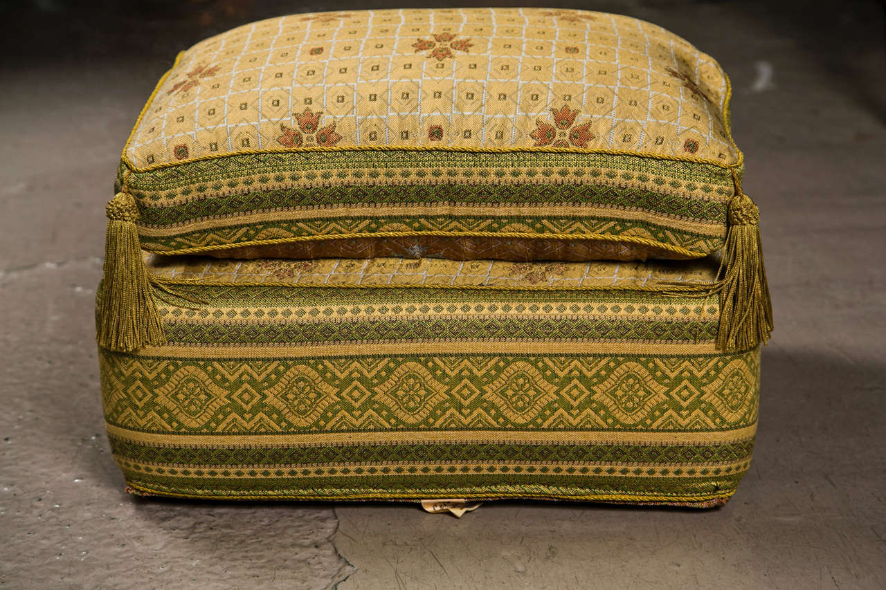 A finely upholstered poof or ottoman.Green and cream with gold fabric the corners all having tassle pulls. Very decorative.