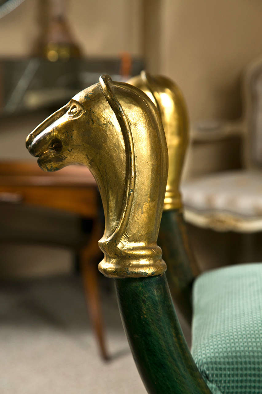 Egyptian Revival style green painted and parcel-gilt Curule form bench, decorated with dog-head motif, padded seat. Attributed to Maison Jansen.