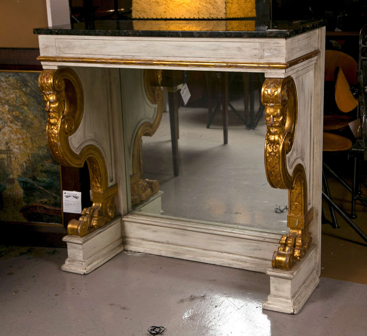French pier console table in the neoclassical style, circa 1950s, the dark charcoal marble atop white distress-painted pedestals decorated with parcel-gilt figural motifs, mirrored backsplat, raised on block plinth.