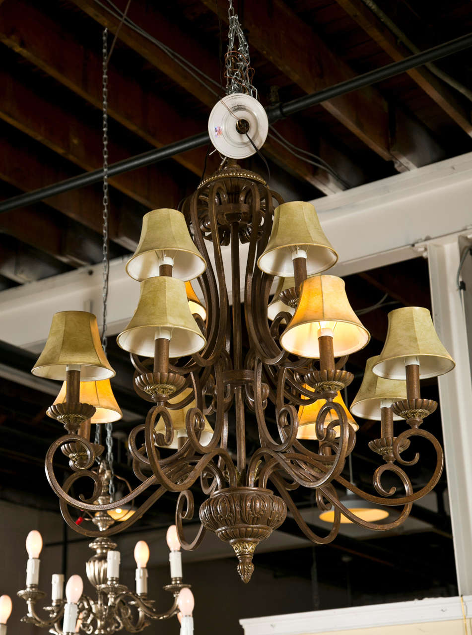 A decorative iron twelve-light chandelier, each light with shade, the bottom decorated with a large finial.