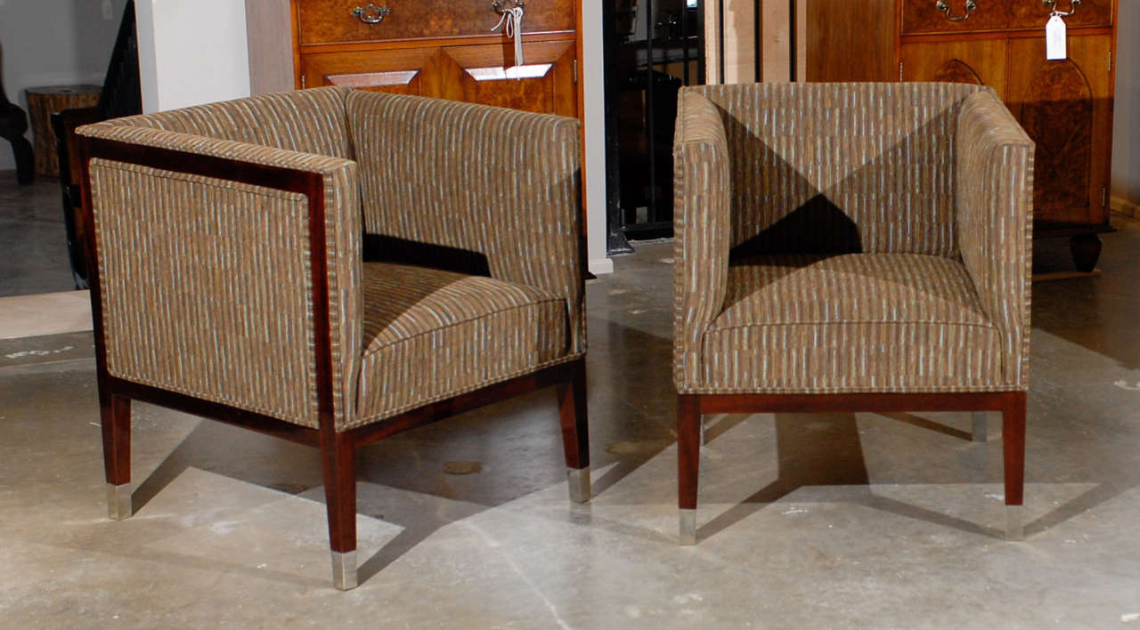 This pair of Art Deco period upholstered club chairs from the first half of the 20th century features square wraparound backs over  mahogany bodies. We are here in the presence of quintessential Art Deco design. The linear silhouette of the backs