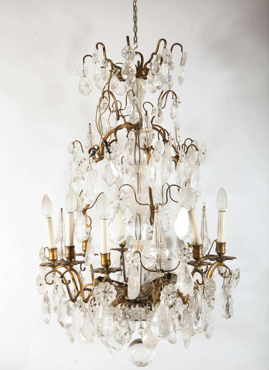 A  Louis XV period gilded bronze rock crystal chandelier with nine scrolled arms in gilded bronze with nine candle lights within bôbeches of floral shaped motif. Faceted diamond and tear shaped rock crystals hang from rosette shaped rock crystals,