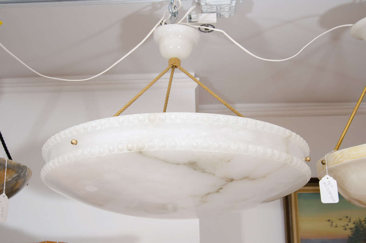 An important fixture by virtue of its size, the creamy white alabaster is lightly veined and features two rings of full beading. Suspended on electrified roping and recently rewired, the fixture holds four 75 watt bulbs.

Custom rewiring to your