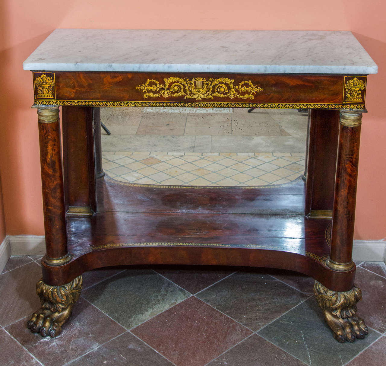 American Empire marble-topped mahogany pier table, the apron with gilt stencil decoration depicting a lyre and fruit baskets, the front column supports with chased bronze mounts, a mirrored back and with a shaped undertier on bold lion paw feet.