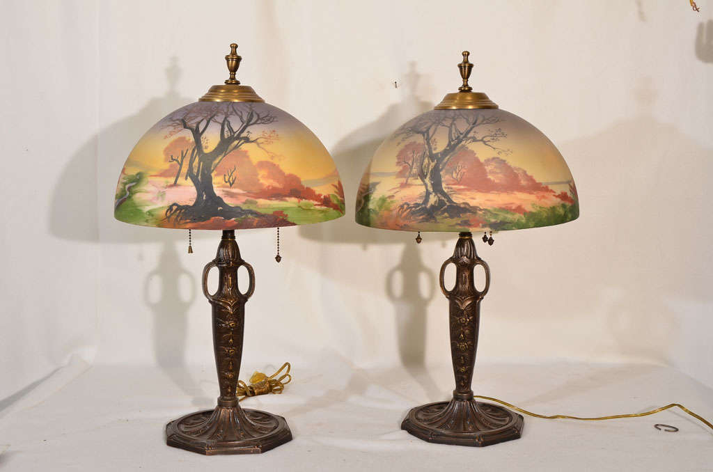 Pair restored to original bronze finish, with roses in relief on the body of the lamps.  Lamps were manufactured by Pittsburg Lamp, Brass and Glass Co in early 1900's.  The shades are obverse painted (on outside of glass) and are not exactly alike