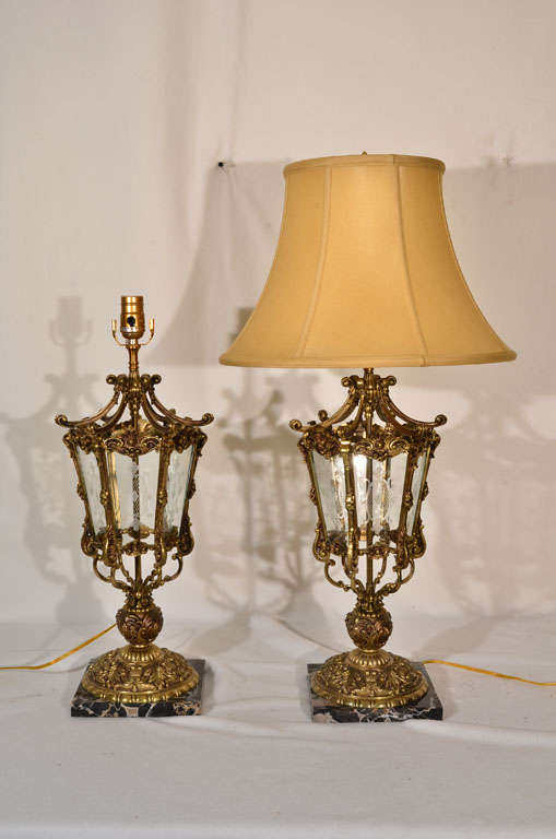 Elegant pair French Neo Classical style, cast bronze table lamps mounted on beautiful black marble with panels of etched and cut glass in the lantern.   Restored to original Finish with new wiring. Lamps are shown with silk shades that are available
