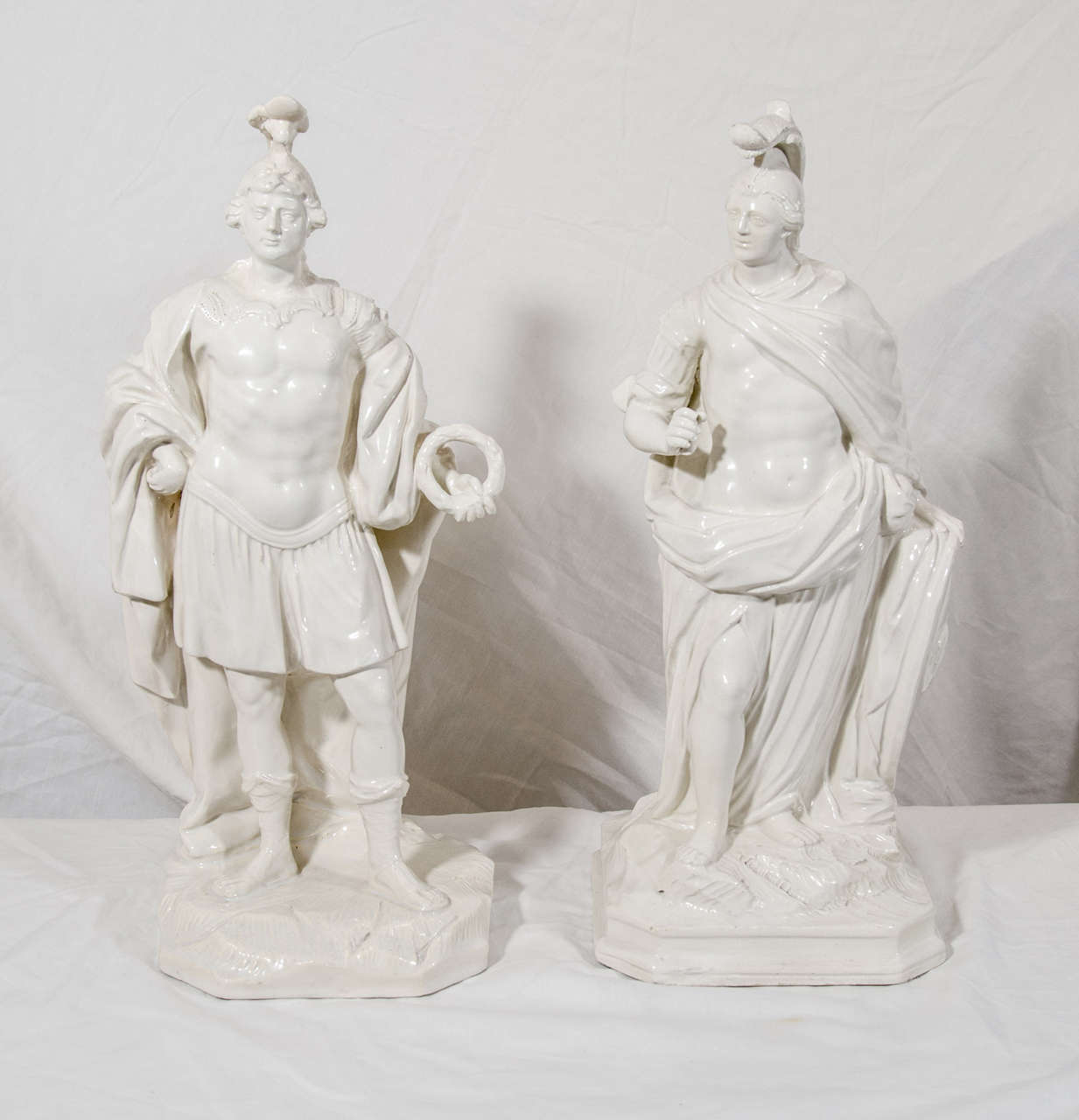 A pair of rare Creamware figures of Roman officers. Each shown standing at rest wearing elaborate headdress and robe indicating high rank. One figure holds a victory wreath, the other rests leaning on his shield.