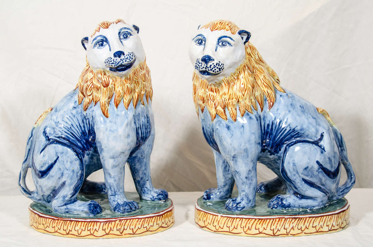A pair of 19th Century French faience lions sejant painted in polychrome colors and seated on oval plinths. Lions traditionally symbolize bravery, valour, strength, and royalty.