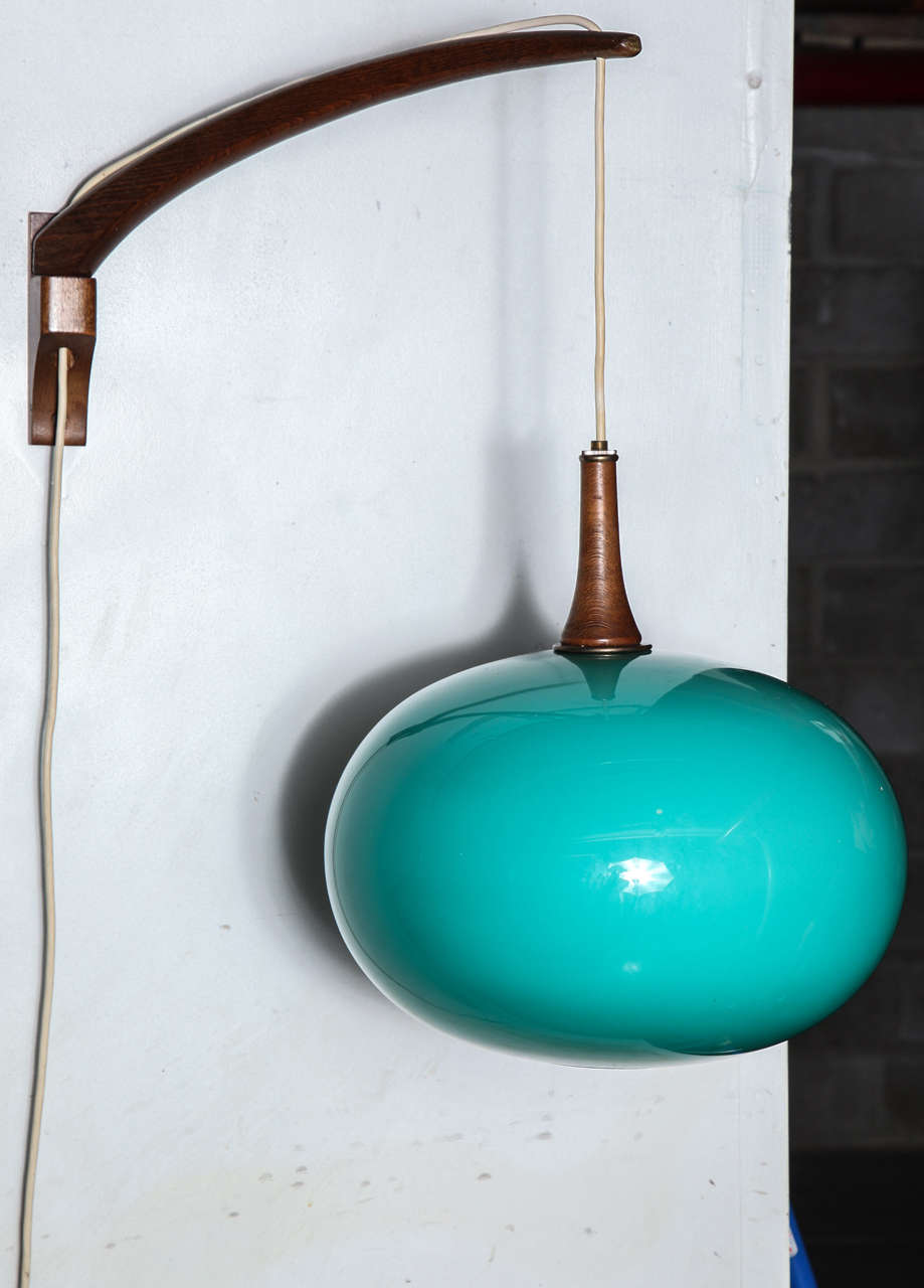 Mid century design at its best, this swing arm wall lamp  also adjusts to change height of shade up and down.  Solid walnut arm and bracket as well as accent above cased blue glass shade.  Arm reach is 10