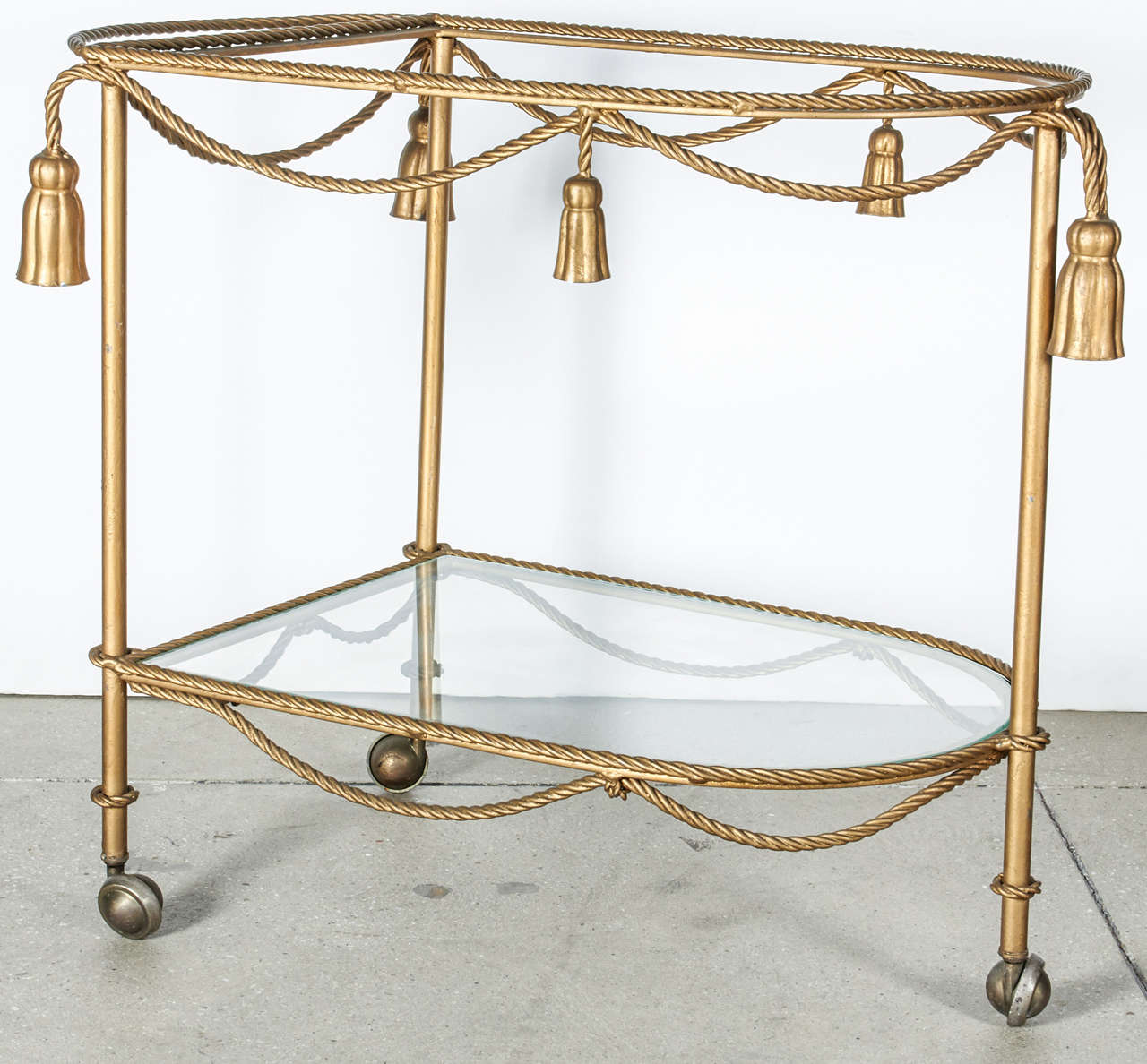 Gilt-metal rope and tassel bar cart.  Italy, circa 1960.  Two available; priced individually.

Features a metal base in gilt metal finish with two removable glass shelves and casters.
