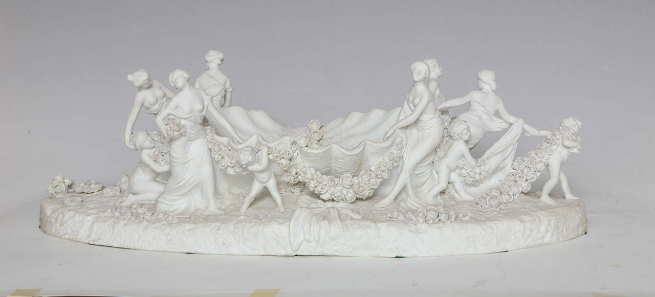 Grand centre de table en porcelaine de Sèvres en biscuit blanc représentant une femme et des enfants. Les femmes et les enfants utilisent les guirlandes de fleurs pour tirer le coquillage géant, créant ainsi des tableaux imparfaitement symétriques.