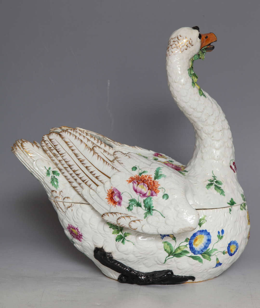 A large 18th century Meissen porcelain covered swan tureen with floral ornamentation. The swan serenely chews a leafy green while turning its head as if to rise. Delicate floral motifs dot the swan's body. Cobalt blue crossed swords mark and incised