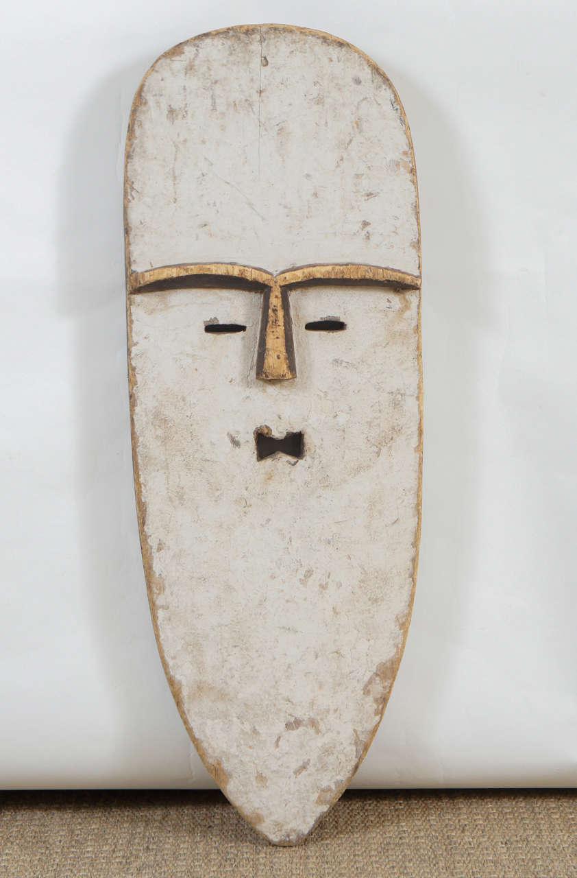 Here is an African carved wood mask with an elongated face finished in white paint.