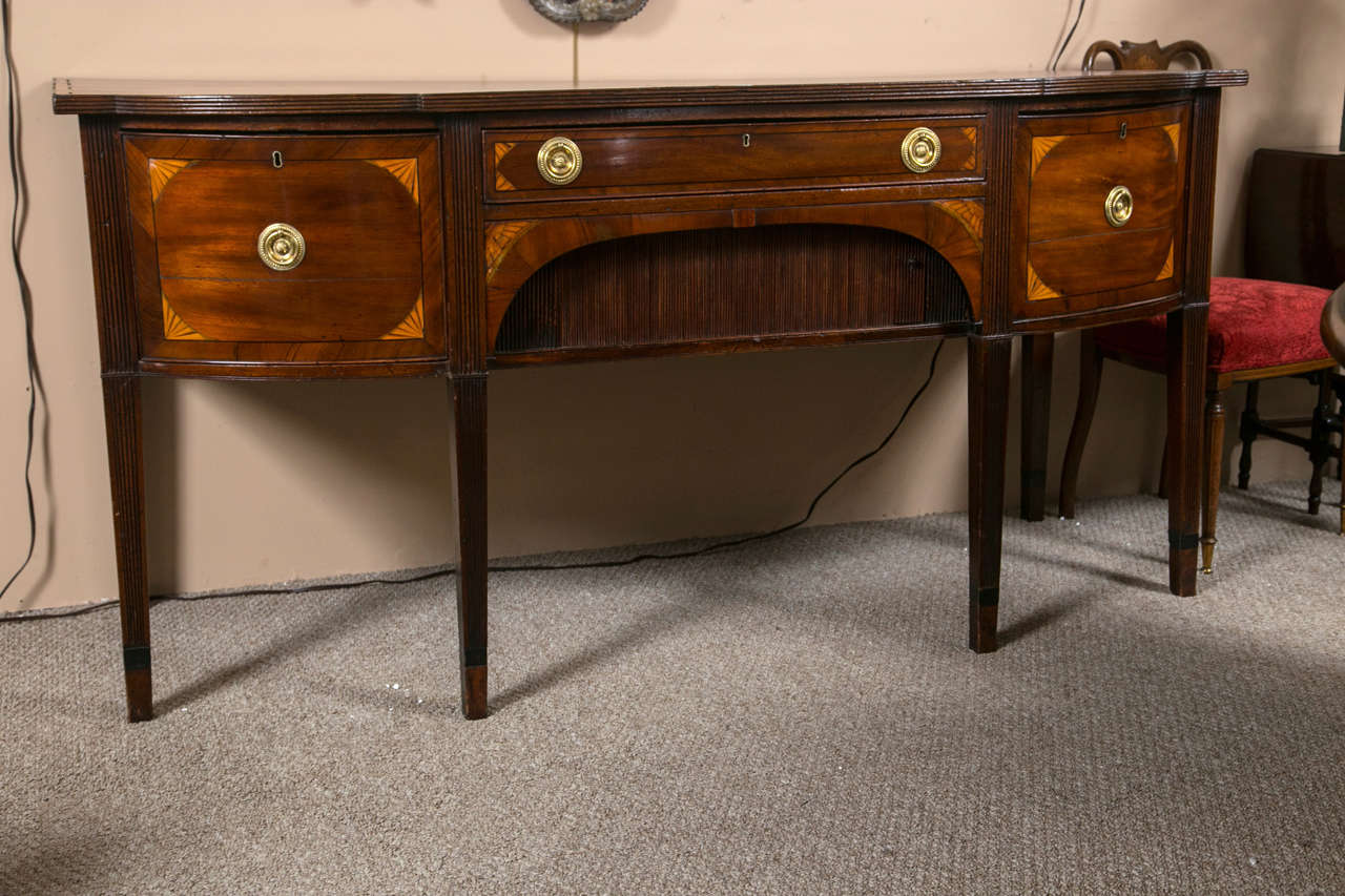 Mahogany Georgian sideboard with fan inlays. This fine sideboard sits on tapering legs supporting an upper case of a center drawer flanked by a pair of fan inlaid side doors with a central sliding tambour door. The top with a wonderful satinwood