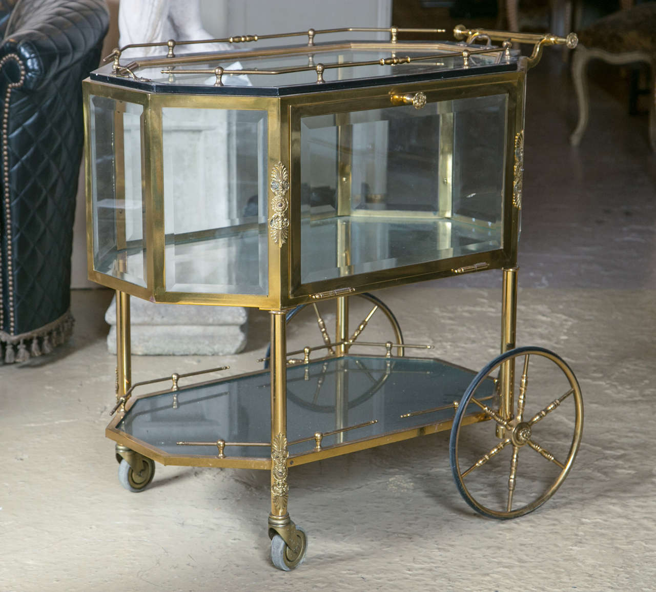 Bronze and glass vitrine serving tea wagon. Large brass wheels make this rolling cart easy to maneuver. The all beveled glass case with pull down side to allow for easy access. The upper and lower with bronze galleries. The whole with a handle for