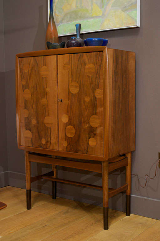 Bar cabinet of walnut by Gustav Bertelsen & Co. Cabinet features two doors concealing a lighted interior with two shallow shelves and one full shelf, two drawers and one pullout
surface. Rear mirror in back of cabinet has been removed.