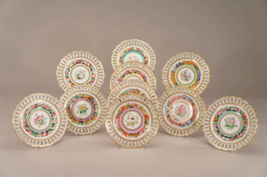 Ce magnifique ensemble de 10 assiettes de cabinet du XIXe siècle présente des motifs arlequins, multicolores et botaniques. Chaque assiette est peinte de manière unique avec un spécimen botanique différent. L'image centrale est un exemple plus grand