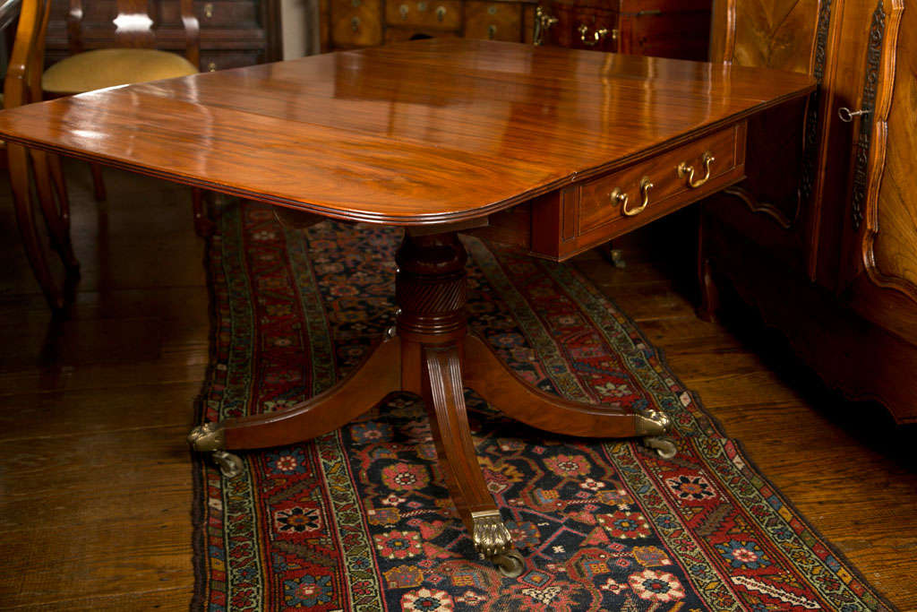 Cette table de canapé à feuilles tombantes en acajou de la fin du règne de George III incorpore des éléments de conception communs à l'époque. La lecture en diagonale sur le piédestal et les pieds poilus en laiton en forme de 