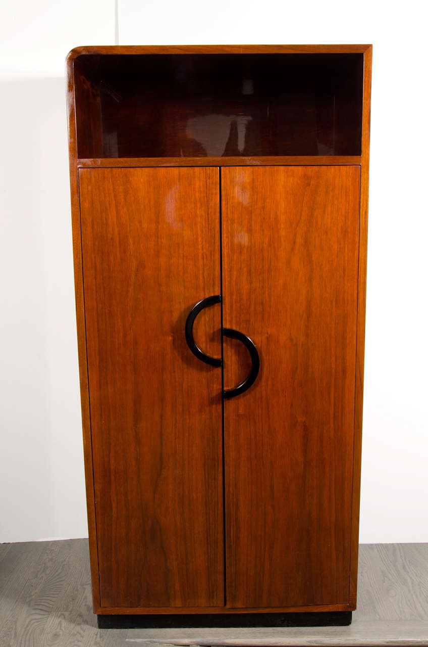 This impressive Art Deco Machine Age cabinet is made of fine book matched walnut and features eight compartments behind the pair of center opening doors and an inset upper niche. The doors feature an off-set pair of semi circle black lacquered